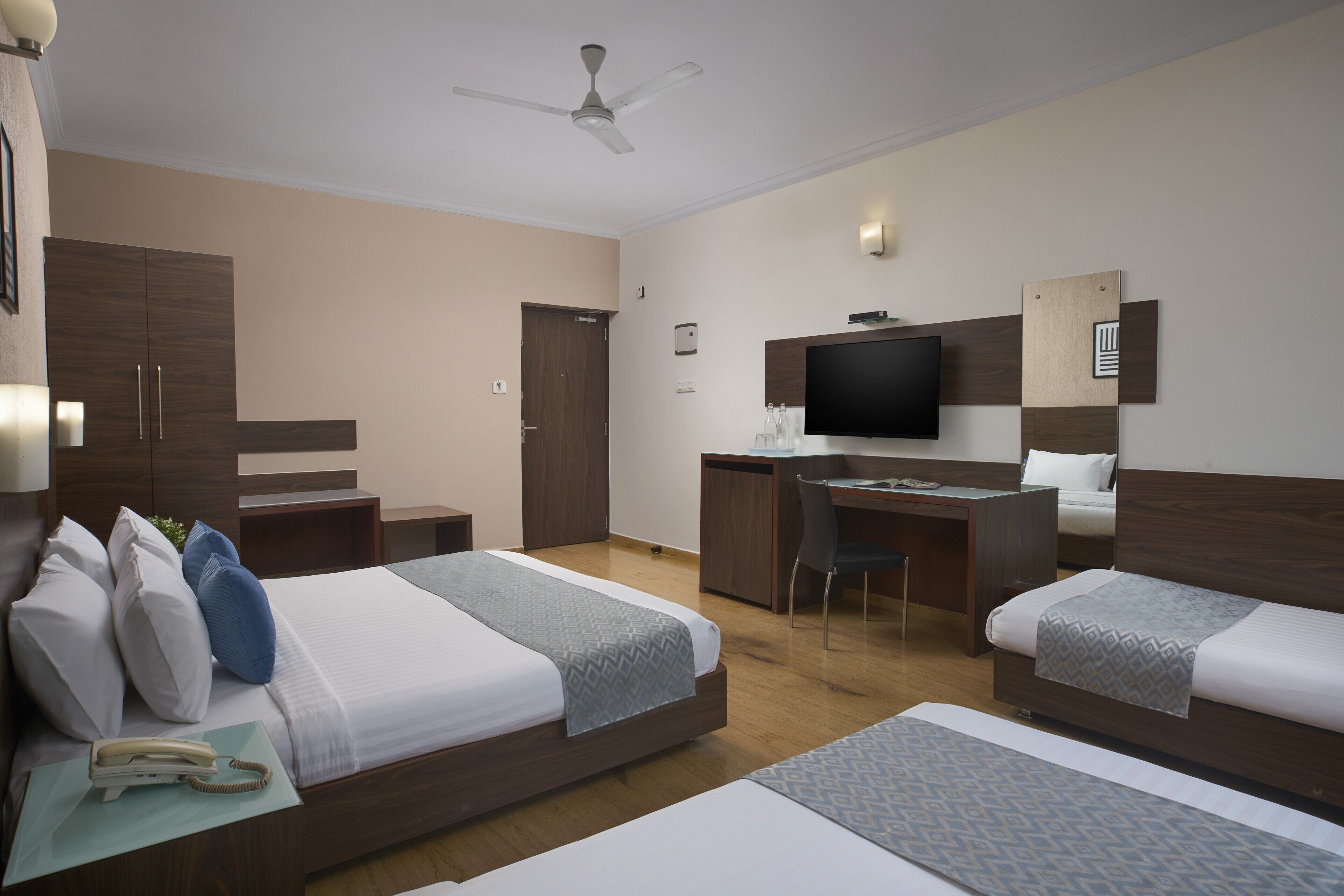 Ein Hotelzimmer mit zwei Betten, einem Schreibtisch, einem Fernseher und einem Deckenventilator.