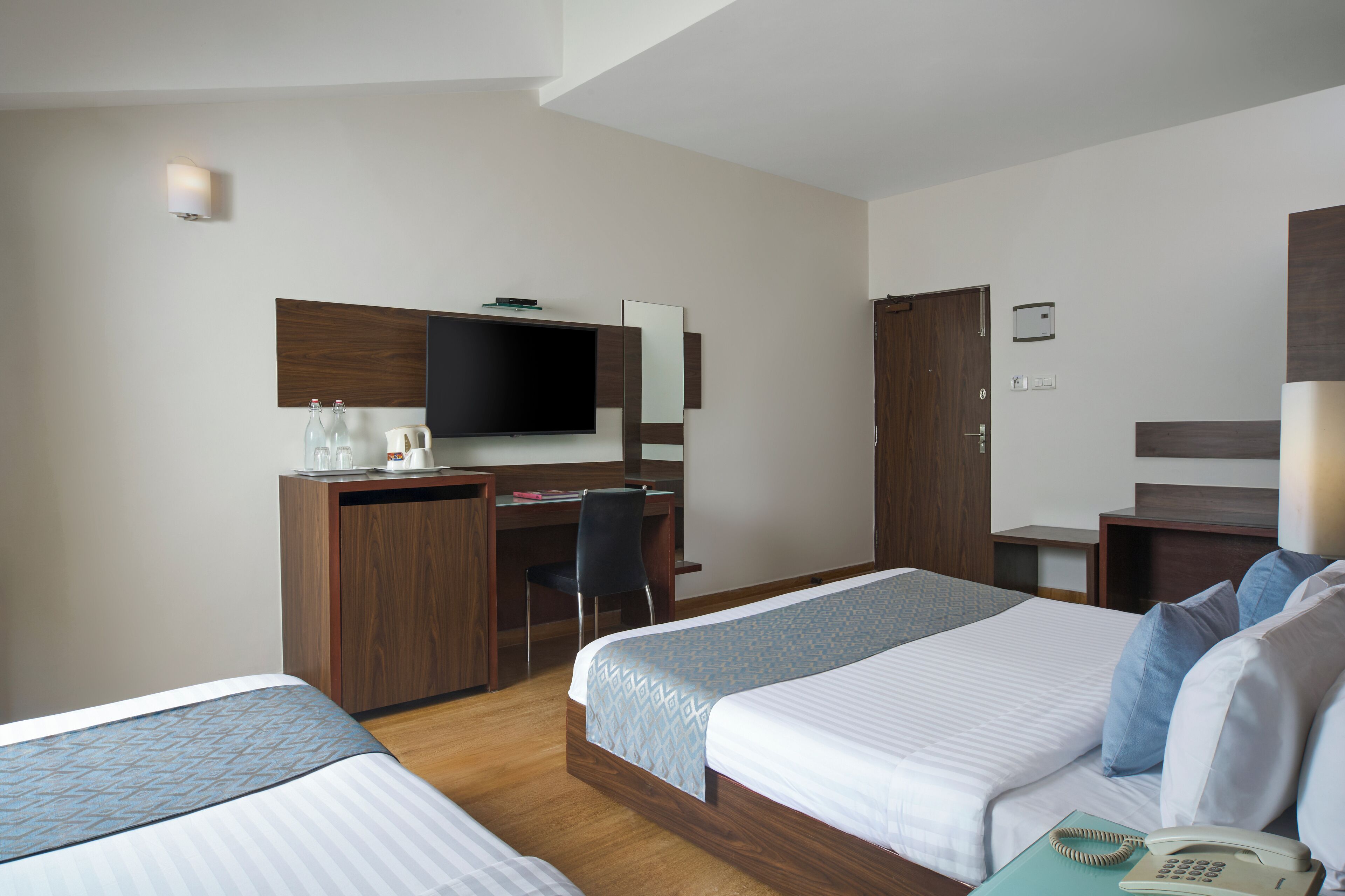 A hotel room with two beds, a desk with a TV, a chair, and a phone on the side table.