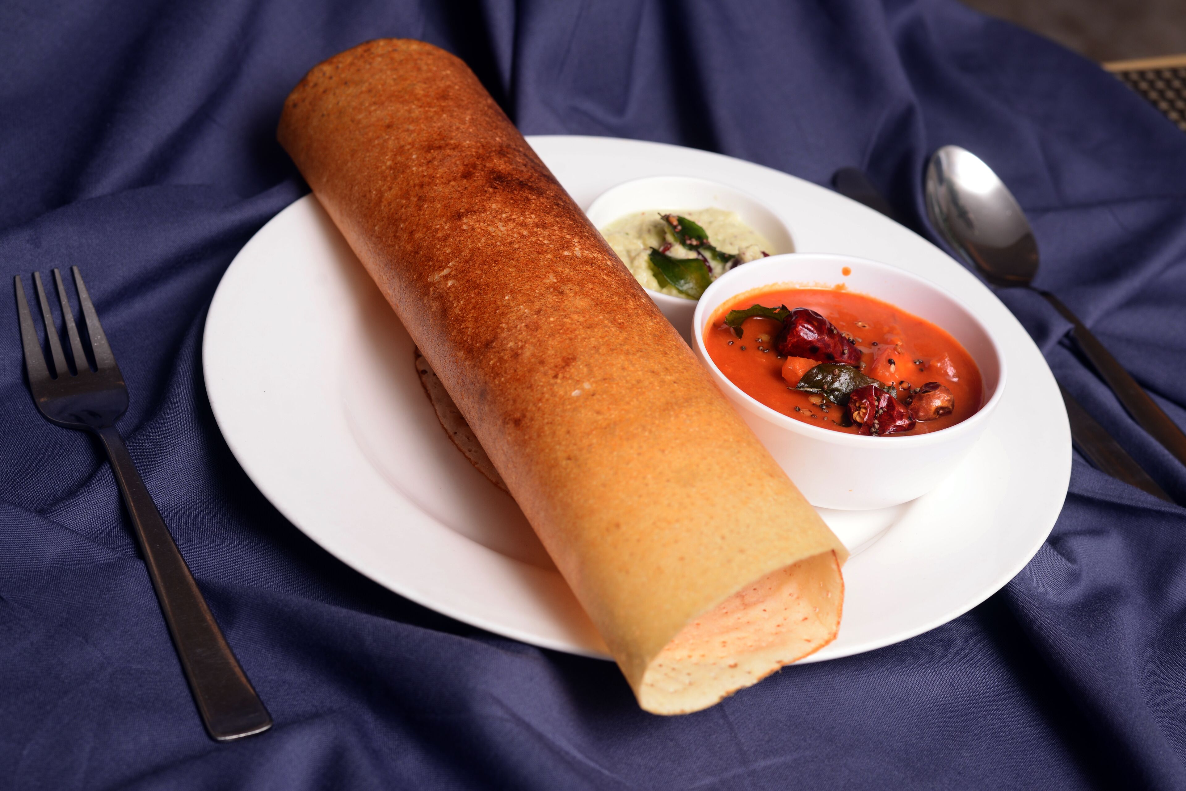 A rolled crepe on a white plate with two small bowls of dips.