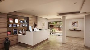 A reception area with a wooden reception desk, framed certificates, and a digital display. - The Hawaii Comforts (Panaji)