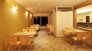 Un comedor de hotel con varias mesas y sillas, un espejo grande y vistas al cielo nocturno a través de las ventanas.