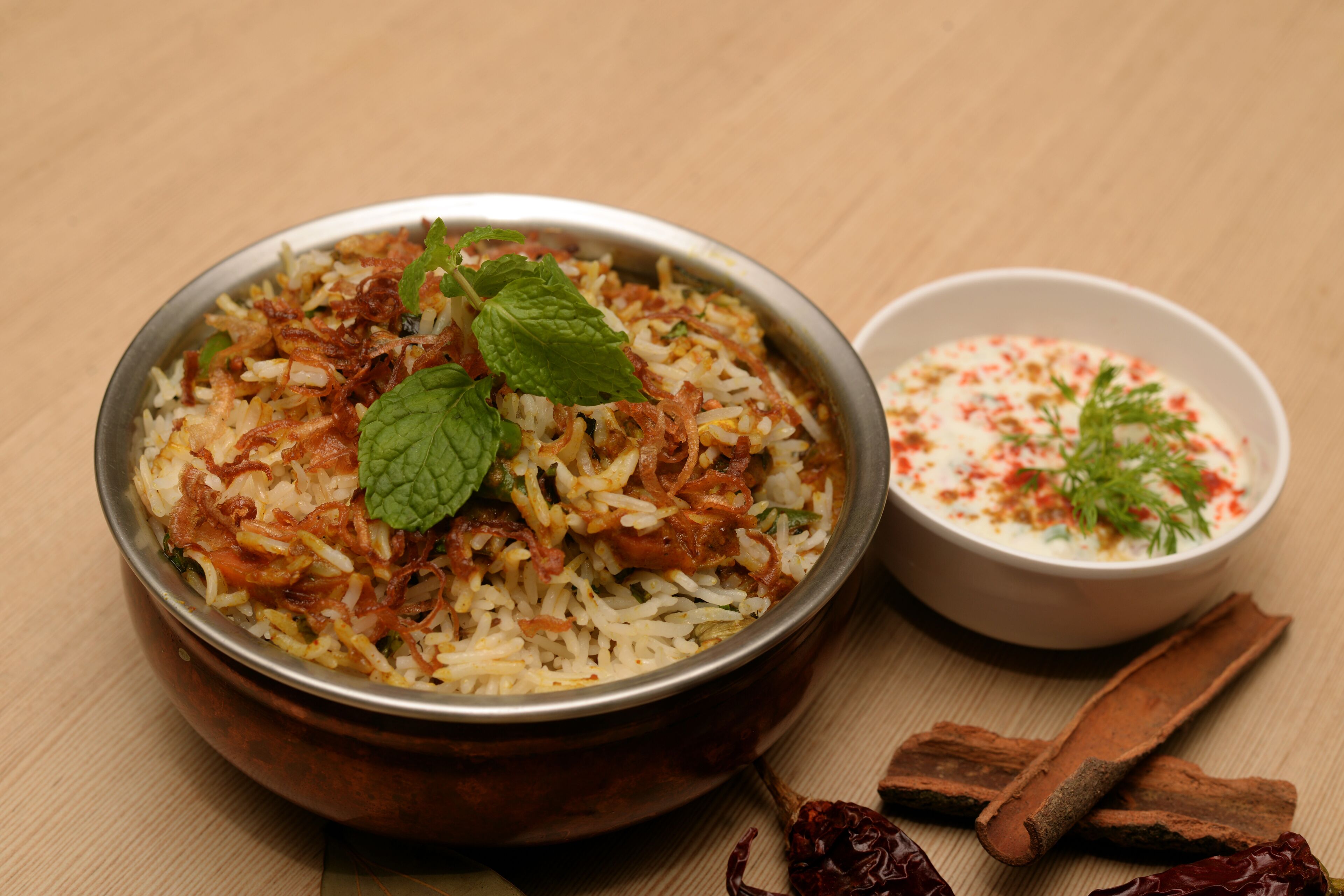 A bowl of biryani with mint leaves and a side of raita.