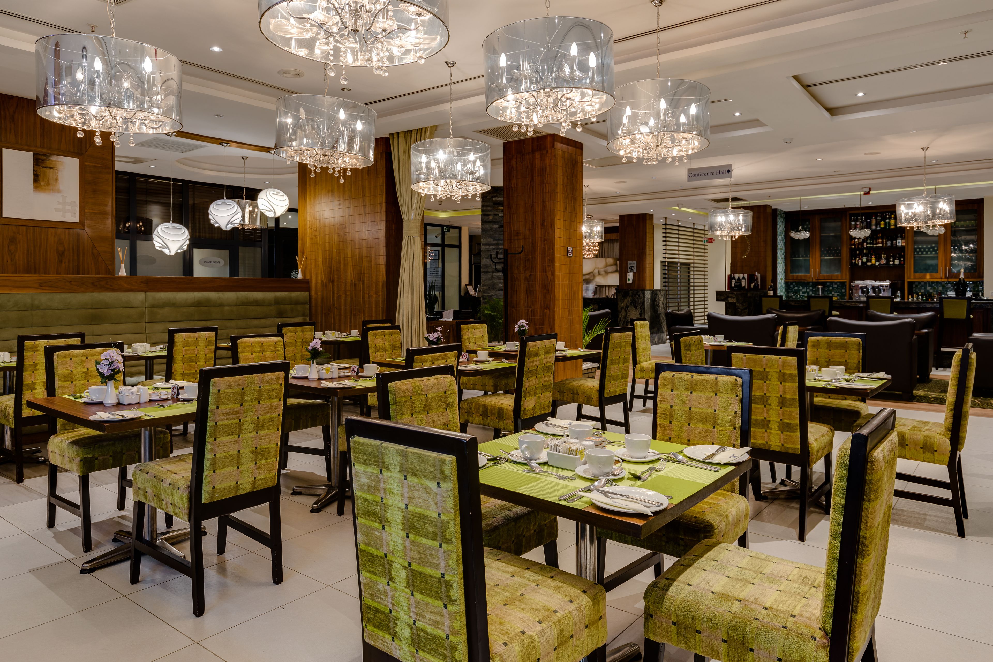 A restaurant with multiple dining tables and chairs, chandeliers, and a bar area.
