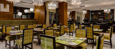 A restaurant with multiple dining tables and chairs, chandeliers, and a bar area.