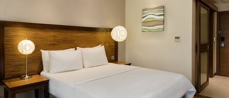 Une chambre d’hôtel avec un grand lit, une tête de lit en bois, deux lampes de chevet et une peinture abstraite moderne accrochée au mur.