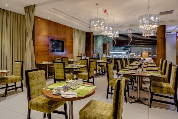 A restaurant with round tables, green upholstered chairs, and chandeliers.