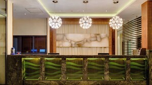 A reception area with a marble counter, green decorative panels, and three chandeliers. - Protea Hotel by Marriott Benin City Select Emotan (Benin City)