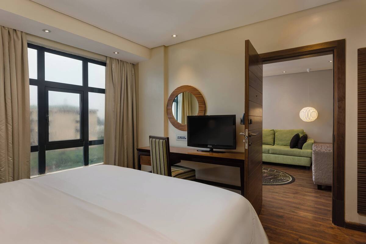 A hotel room with a large bed, a desk with a TV, a green sofa, and a mirror on the wall.