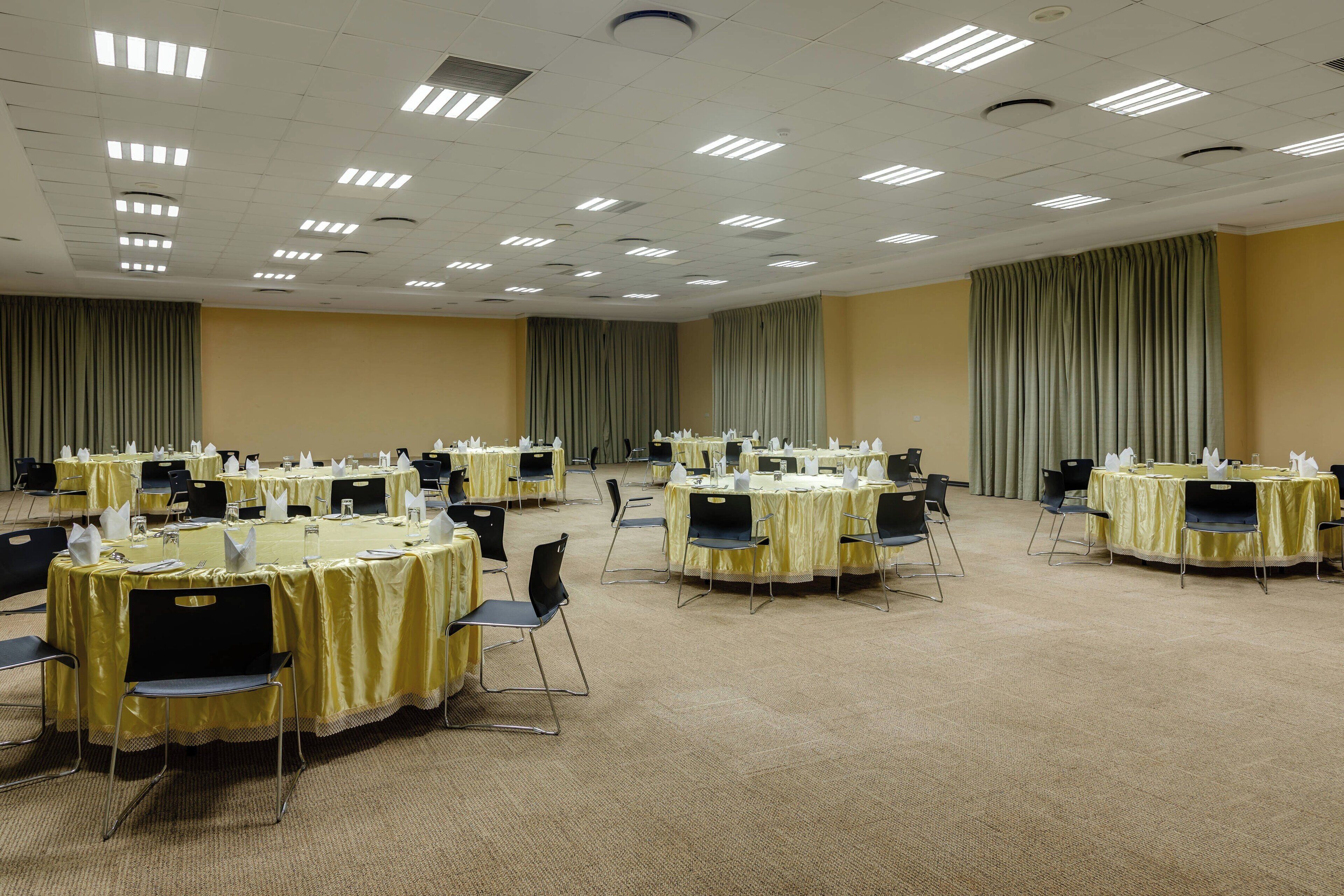 Un salón de conferencias con varias mesas redondas, cada una cubierta con un mantel amarillo y equipadas con sillas y vasos de agua.