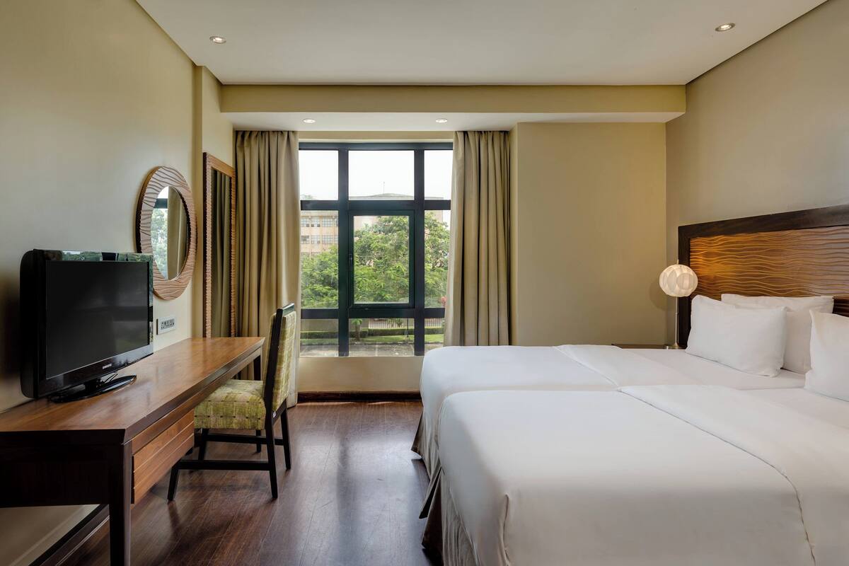 A hotel room with a bed, a desk with a television, a chair, and a window with curtains.