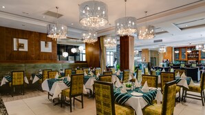 A restaurant with multiple tables set for dining, featuring a mix of wooden and upholstered chairs, and a bar area in the background. - Protea Hotel by Marriott Benin City Select Emotan (Benin City)