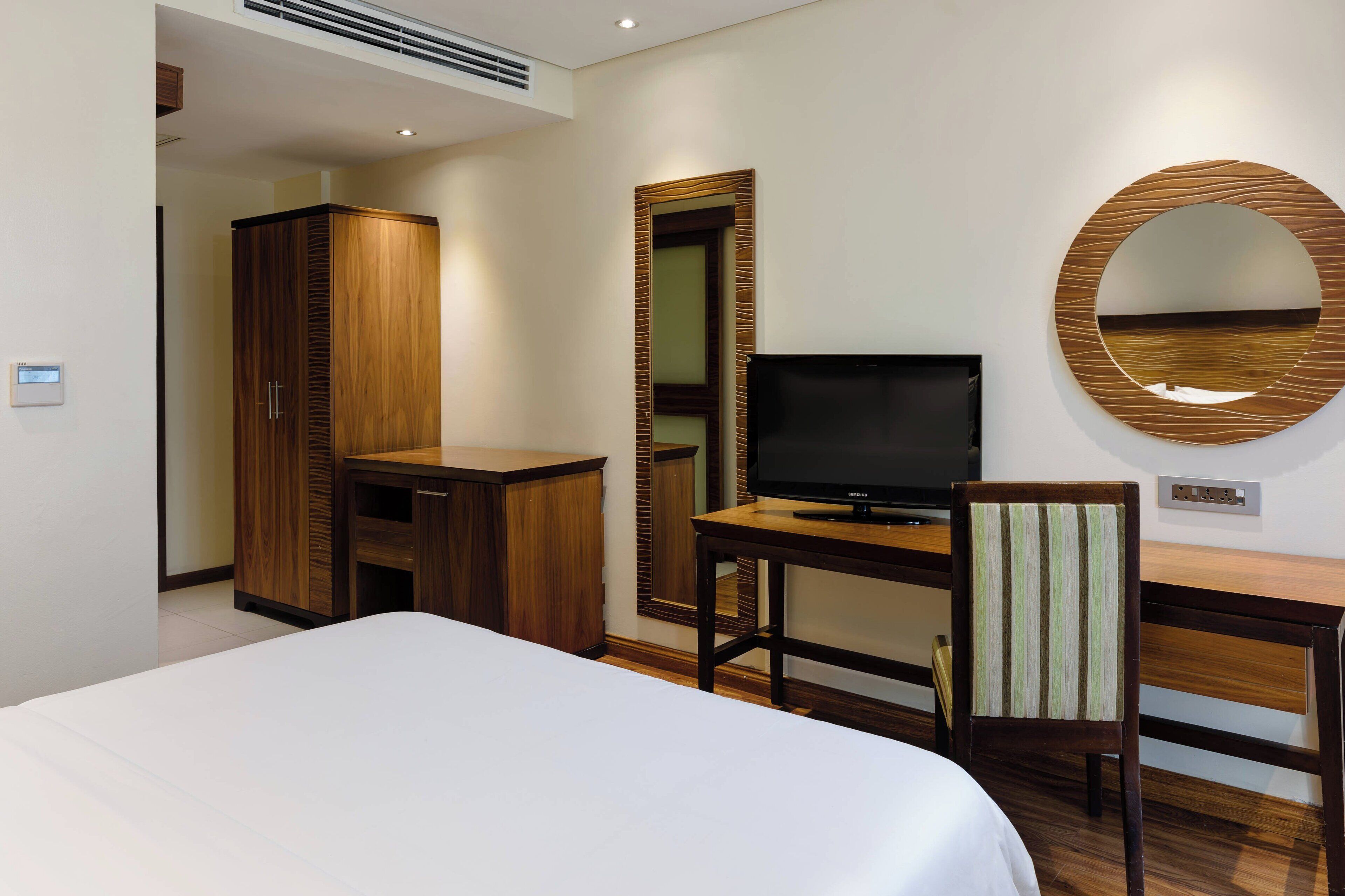 A hotel room with a bed, a desk with a television, a mirror, and a wardrobe.