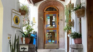 A wooden door with a glass panel, flanked by potted plants and a hand sanitizer sign. - Kituandes Hotel (Quito)