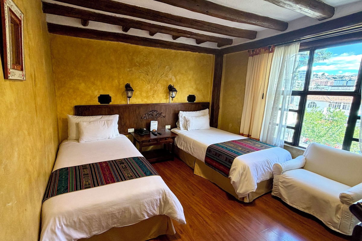 Een hotelkamer met twee bedden, een houten vloer, een groot raam met uitzicht en een wand met een decoratief bladmotief.