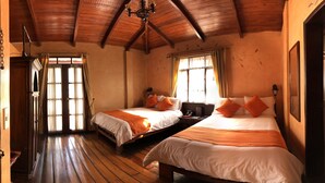 A room with two beds, wooden floors, a wooden ceiling, and a window with curtains. - Kituandes Hotel (Quito)
