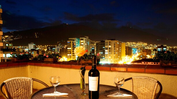 A table with a bottle of wine and two glasses, overlooking a cityscape at night. - Kituandes Hotel (Quito)