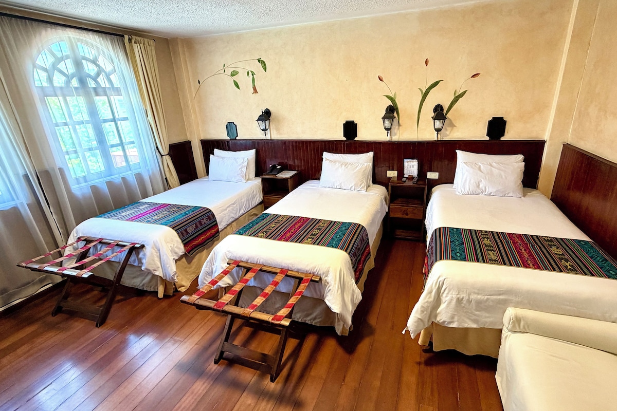 Een hotelkamer met twee bedden, een houten vloer, een raam met gordijnen en wandlampen.