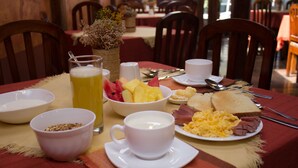 A breakfast setting with a table set for two, including plates of eggs, toast, and fruit, a glass of juice, and a cup of coffee. - Kituandes Hotel (Quito)