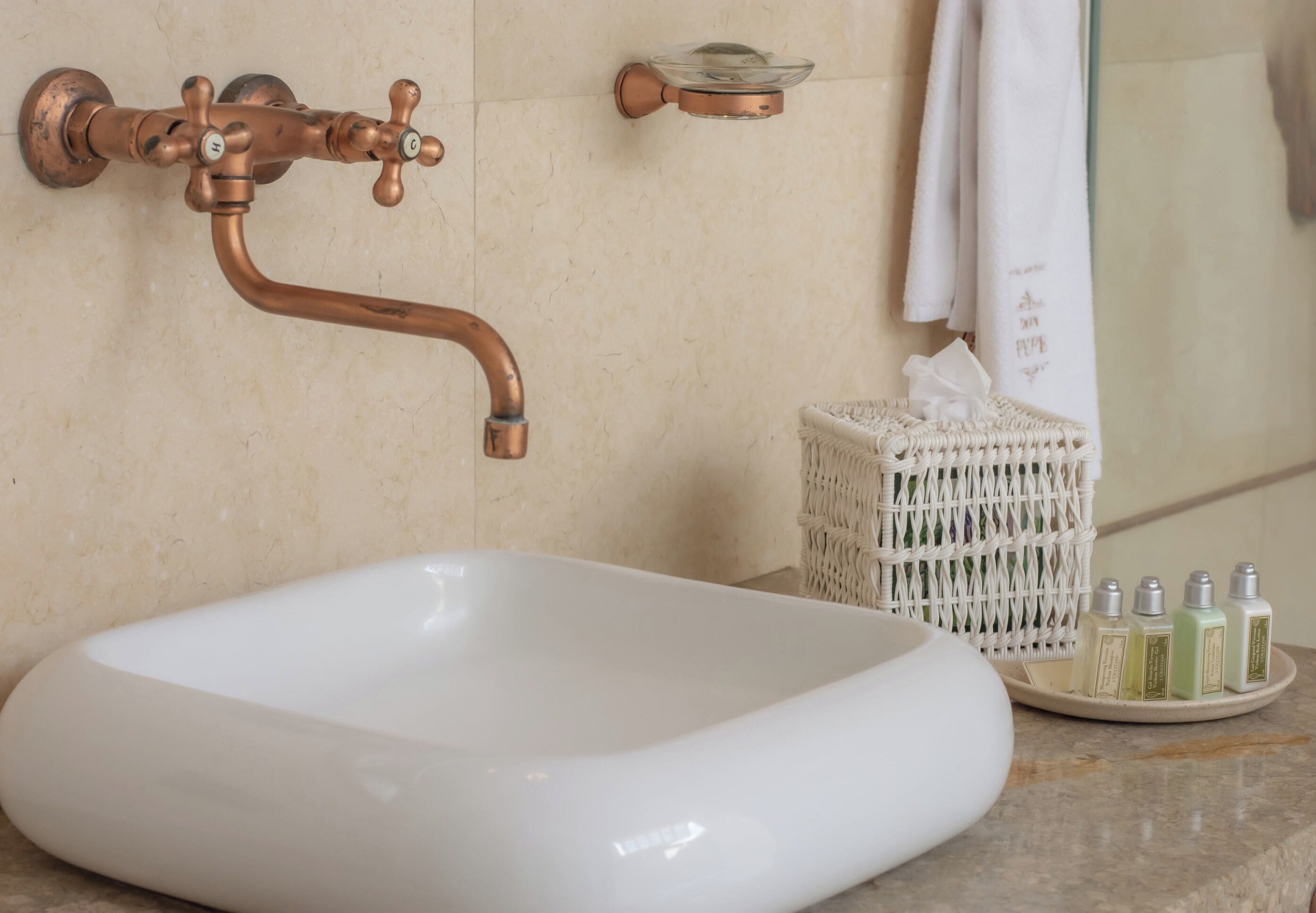 A bathroom with a white sink, copper fixtures, a woven basket, and toiletries.