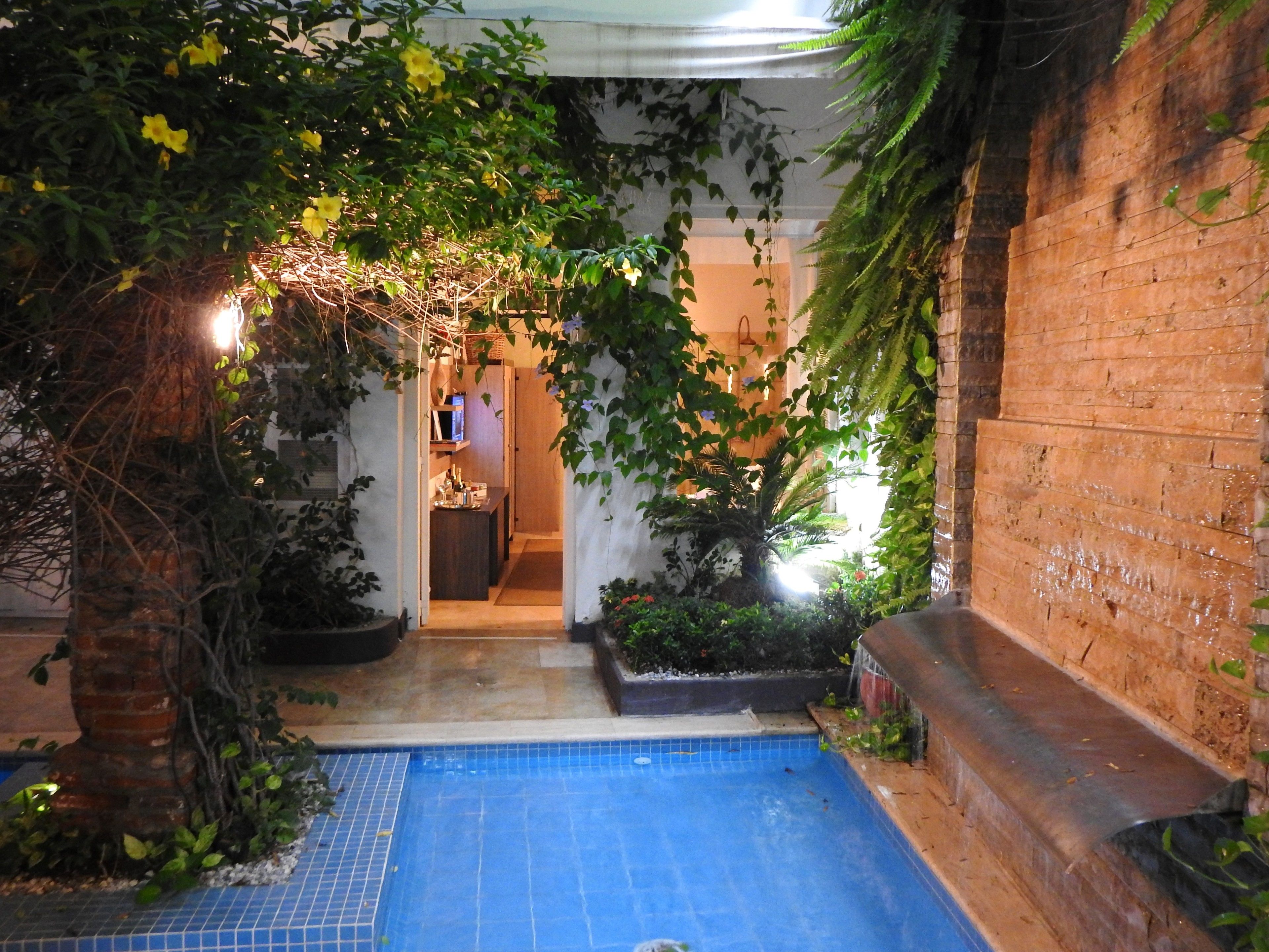 Un espace piscine doté d’un sol carrelé, entouré de plantes et bordé d’un mur en briques.