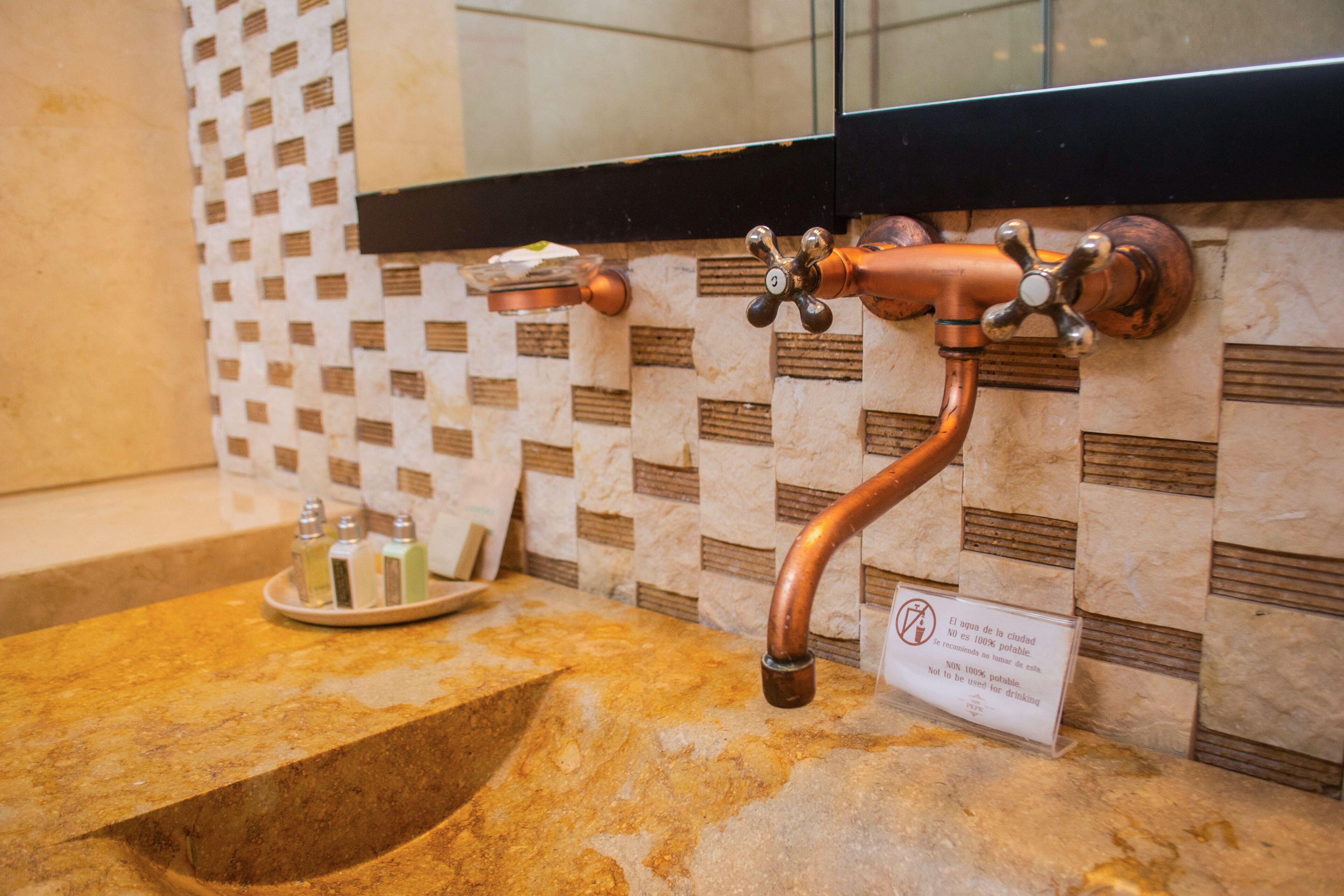 A bathroom sink with a copper faucet, a soap dish, and a sign indicating water restrictions.