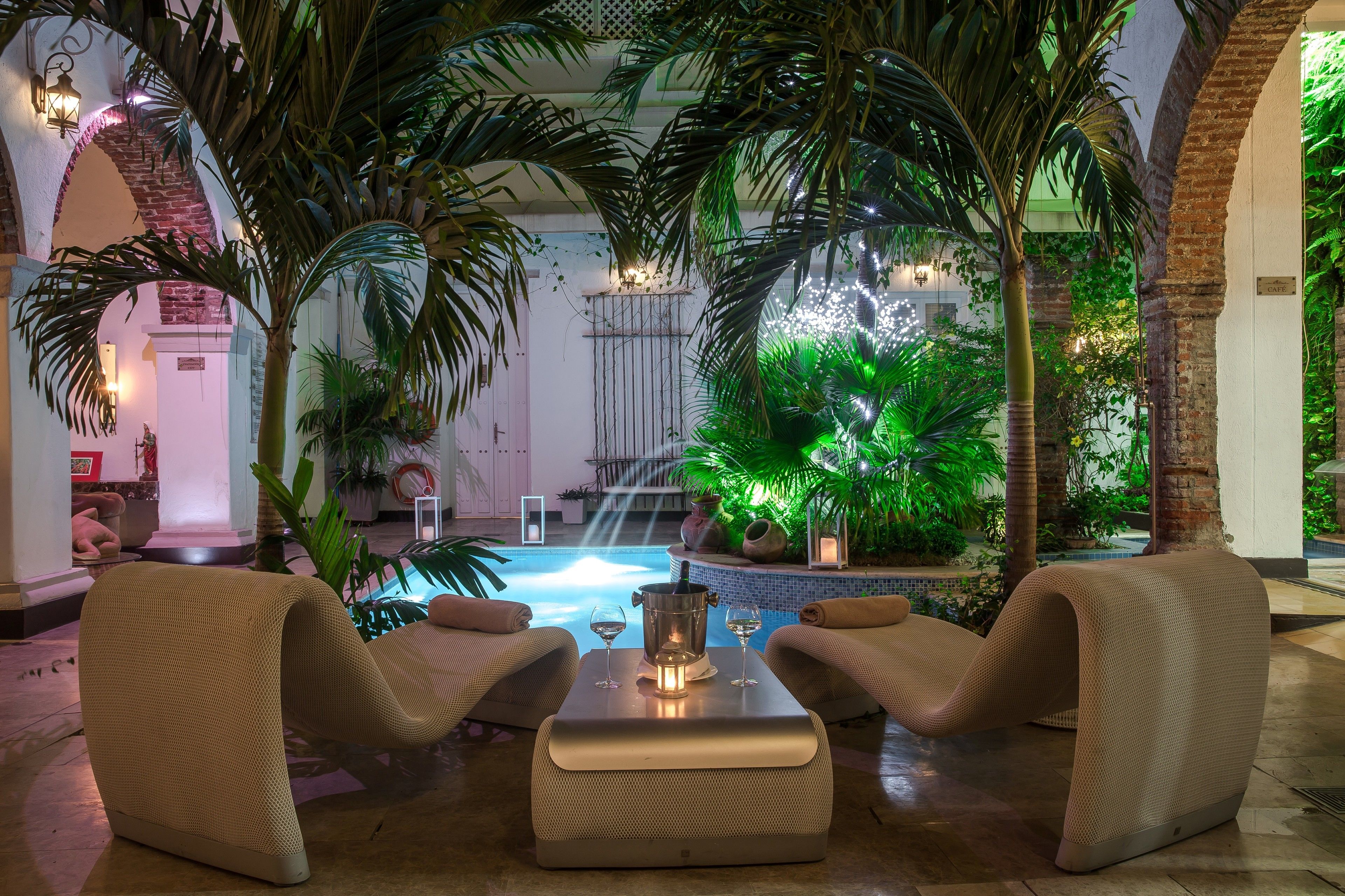 Un salon au bord de la piscine, avec deux fauteuils confortables, une petite table sur laquelle se trouvent une bouteille et un verre, et une piscine agrémentée d’une cascade.