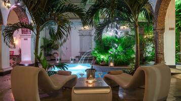 Un salon au bord de la piscine, avec deux fauteuils confortables, une petite table sur laquelle se trouvent une bouteille et un verre, et une piscine agrémentée d’une cascade.