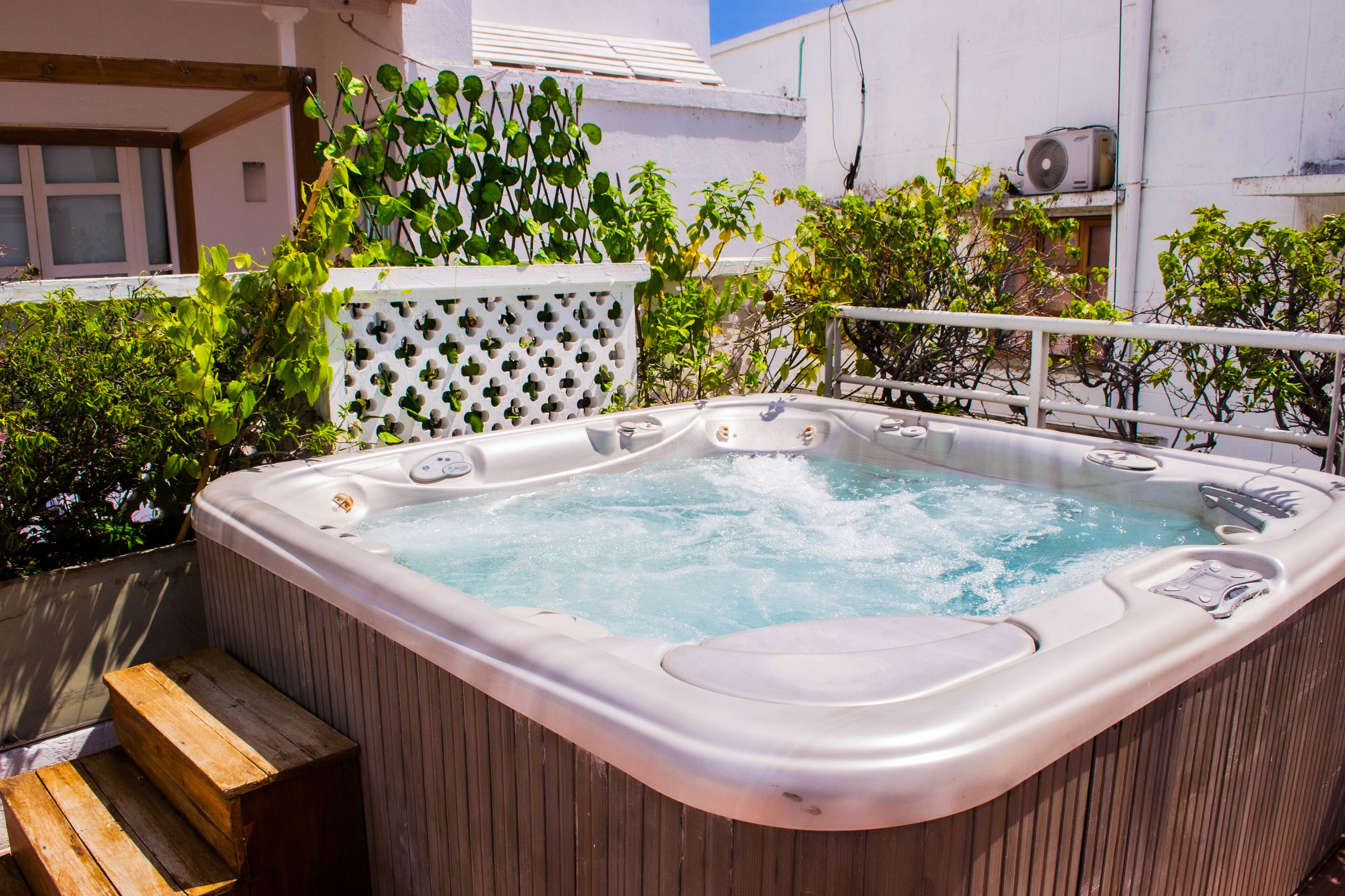 A hot tub with a wooden bench and a white lattice fence.