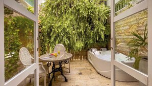 Un jardín privado con una mesa redonda, dos sillas de mimbre, un jacuzzi y abundante follaje.