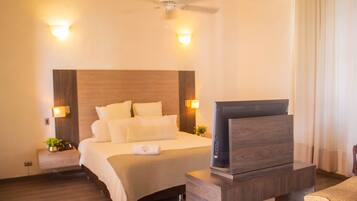 A hotel room with a bed, a TV on a wooden stand, a ceiling fan, and wall-mounted lights.