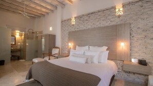 Un dormitorio con una cama grande, cabecera de madera, pared de piedra y una mesita de noche con lámpara.