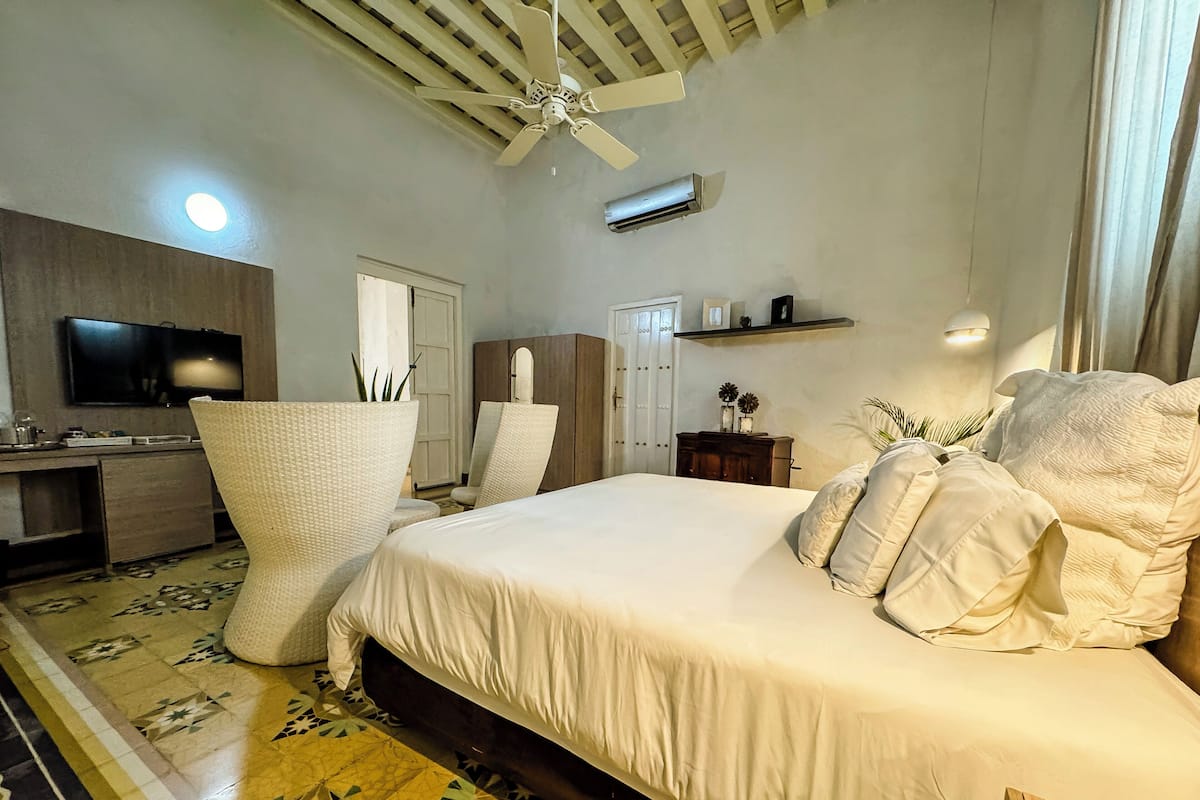 A bedroom with a large bed, a ceiling fan, a TV, and a desk.