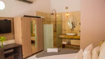 A modern bathroom with a glass shower enclosure, a vanity with a mirror, and a flat-screen TV mounted on the wall.