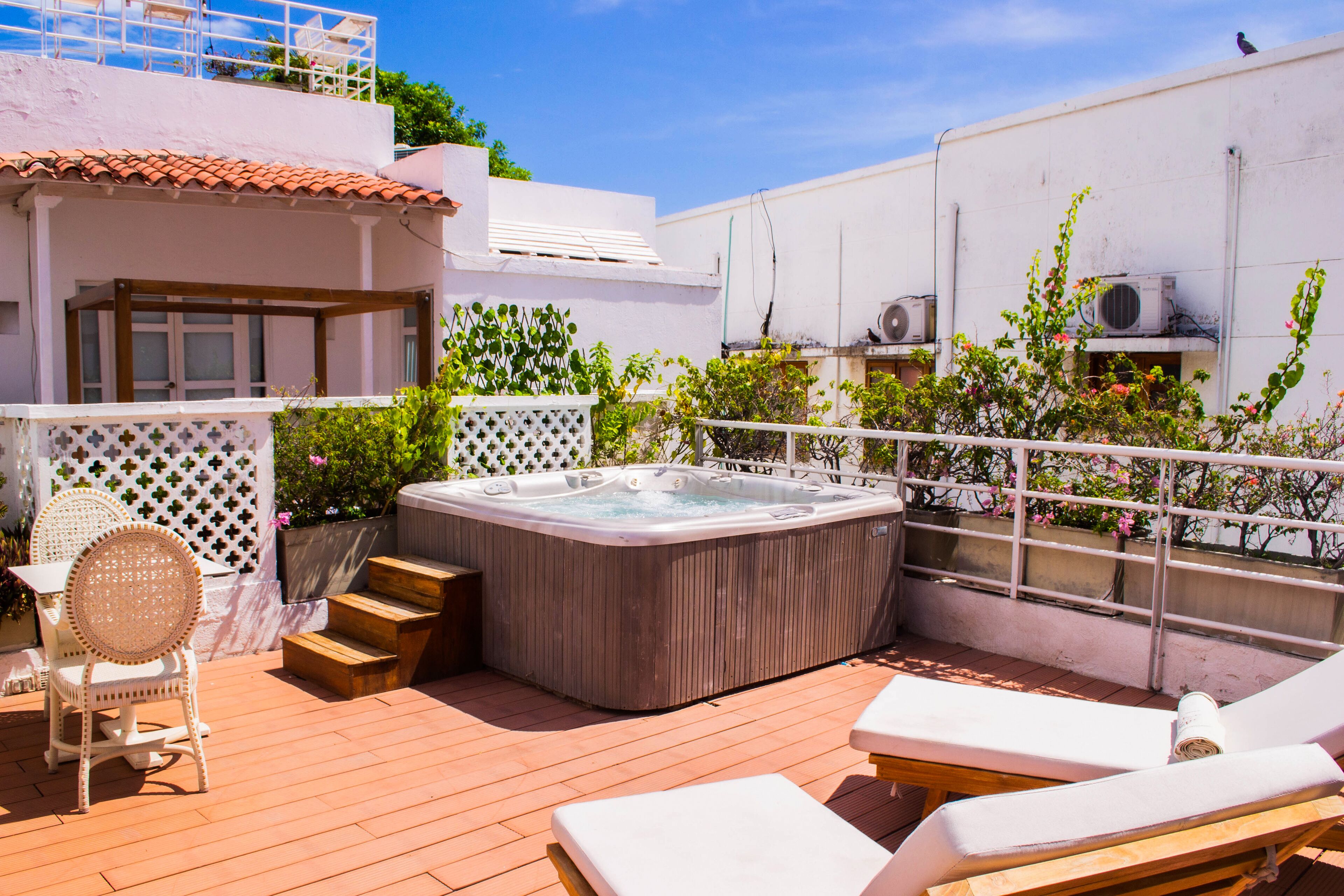 A rooftop patio with a hot tub, lounge chairs, and a dining area with a table and chairs.