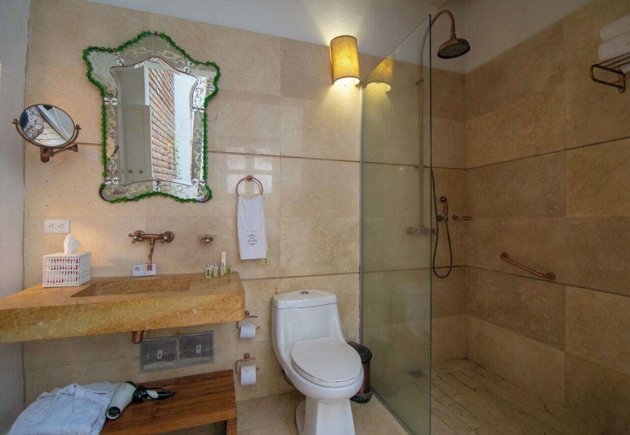 Et badeværelse med en trævådestand, toilet, brusekabine i glas og et spejl med grøn ramme.