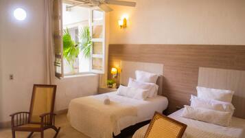 A hotel room with a bed, a rocking chair, a ceiling fan, and a window with a view of greenery.