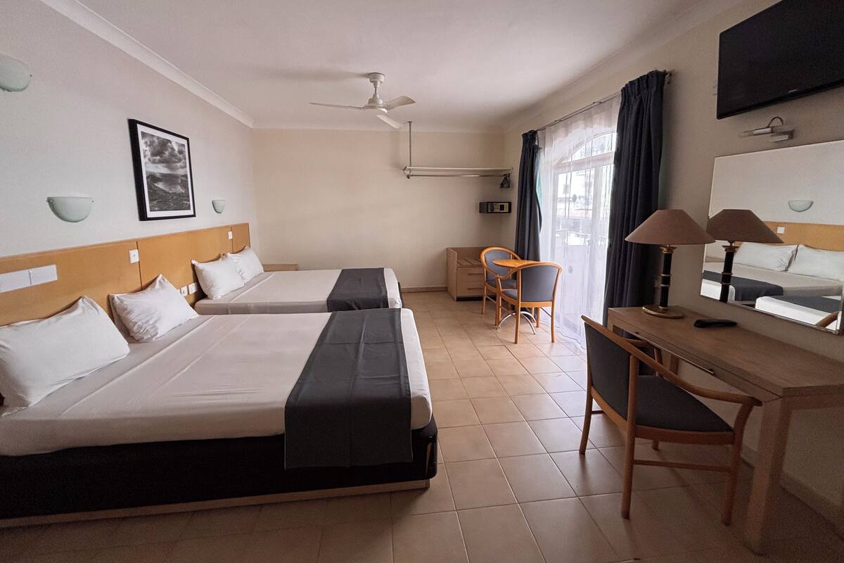 Une chambre d’hôtel avec deux lits, un bureau, une chaise, une télévision et un ventilateur de plafond.