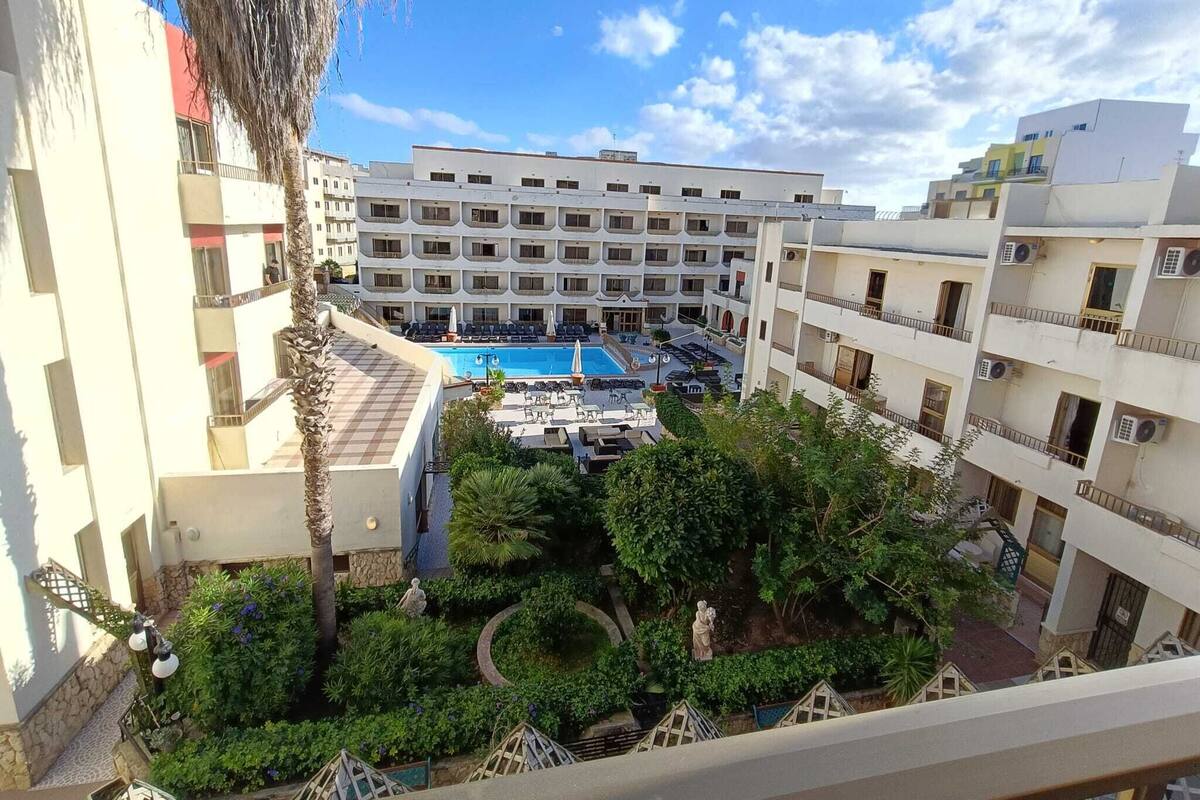 Un hôtel à étages, doté d’une piscine et d’un jardin aménagé avec des statues.