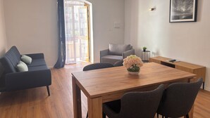 Un salon moderne avec une table à manger en bois, deux canapés, un fauteuil gris et une petite table d’appoint agrémentée d’une plante.