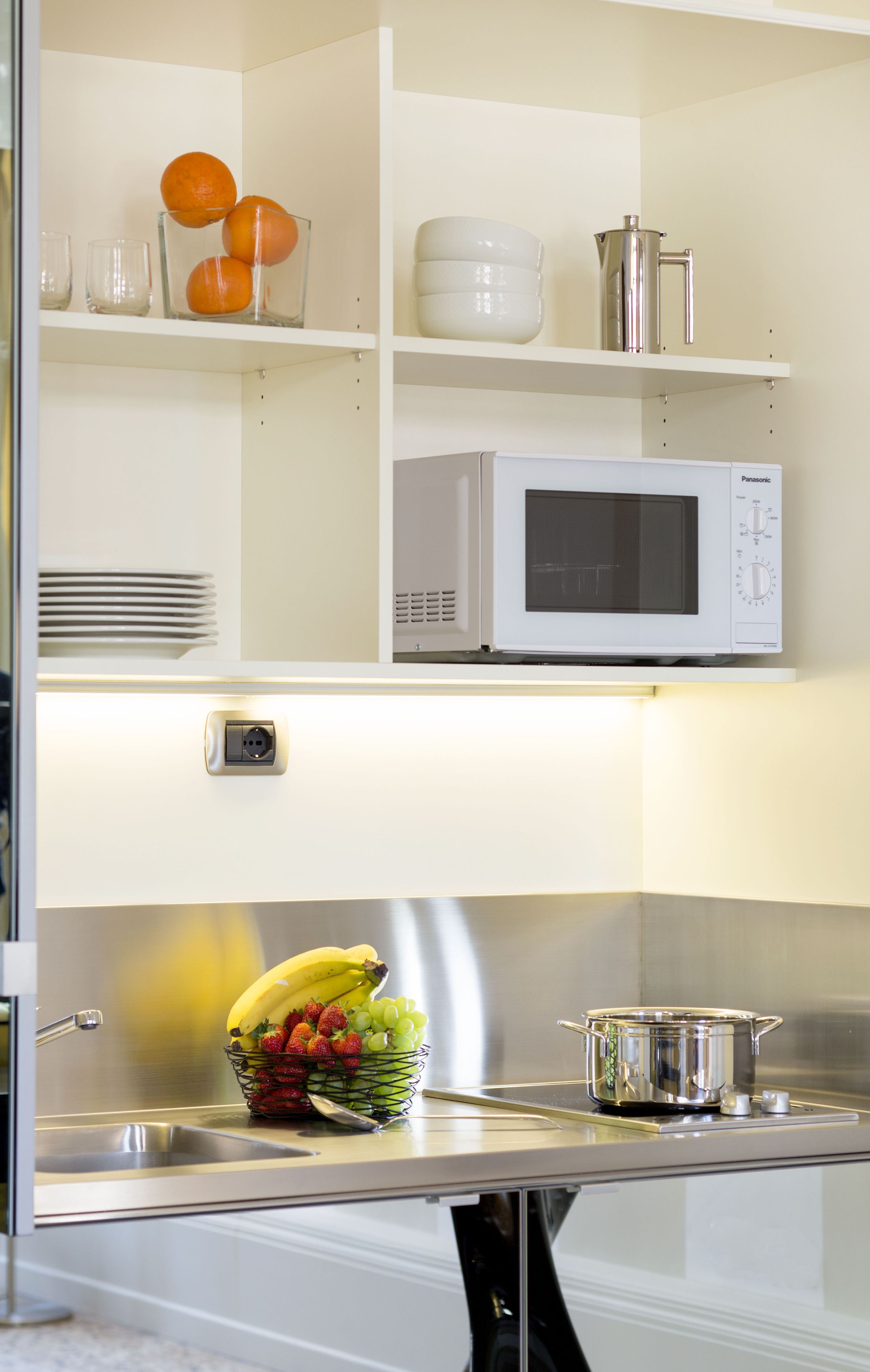 Una cucina con un forno a microonde, una ciotola di frutta e un lavello.