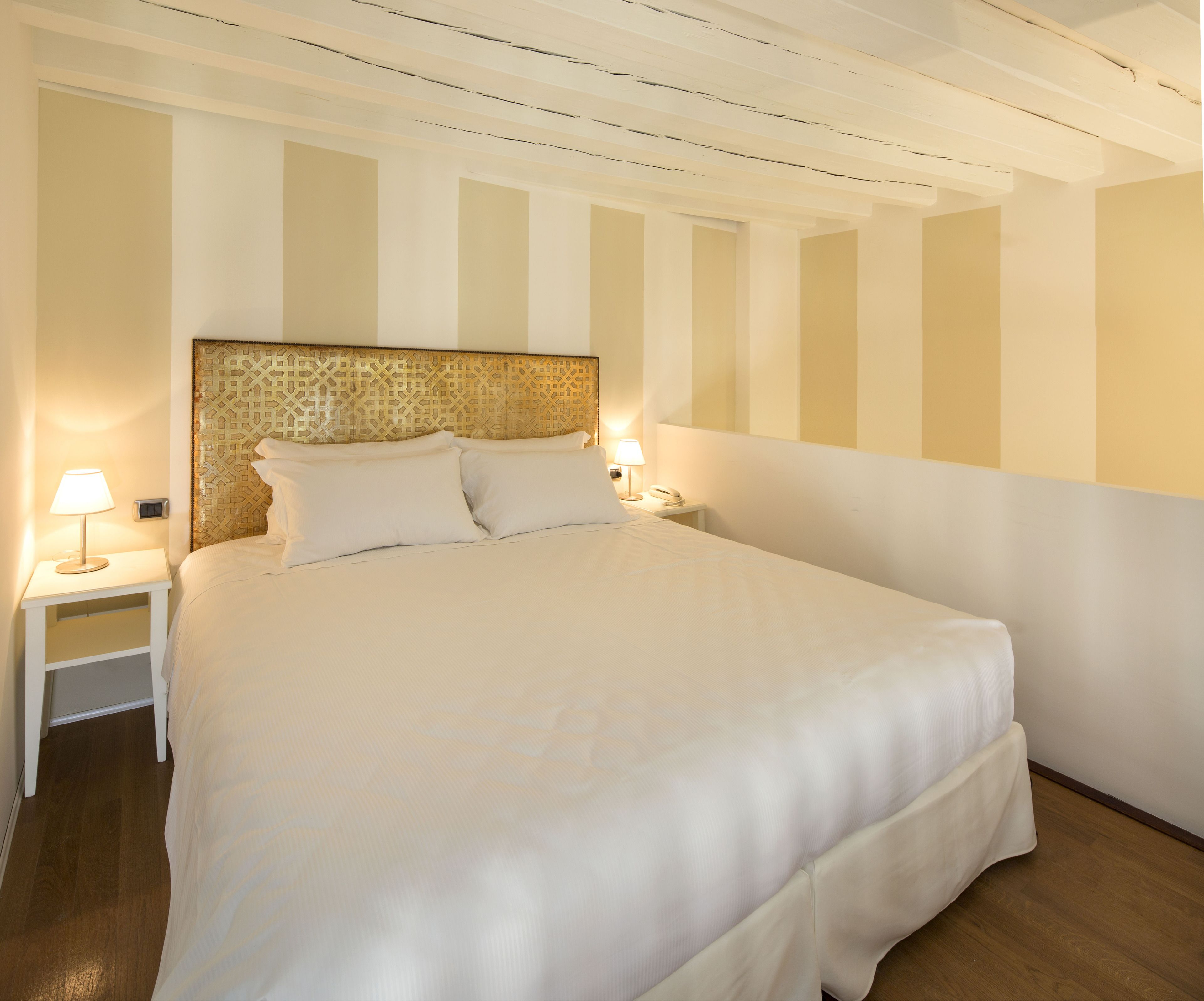 Una cama bien tendida con sábanas blancas, un cabecero estampado y dos lámparas de noche.