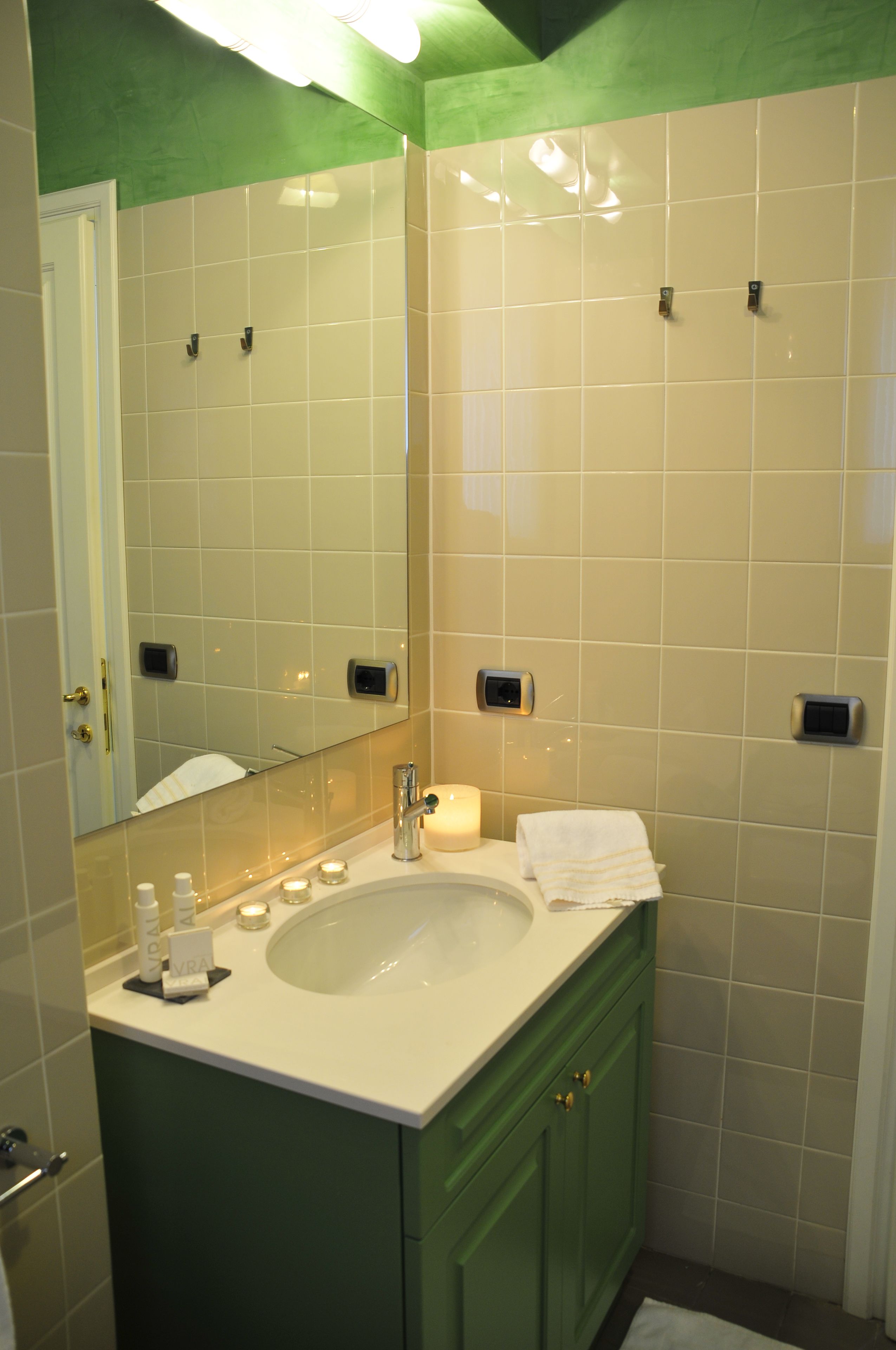 A bathroom with a large mirror, a sink, and a green vanity. There are toiletries on the sink and a towel on the counter.