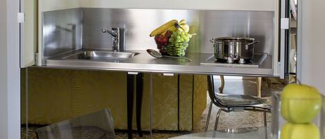 Cocina compacta con microondas, lavabo y un bol de fruta en la encimera.