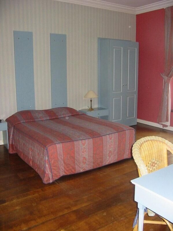 Un dormitorio con dos camas, una mesita de noche, una lámpara, un armario y una silla de mimbre.