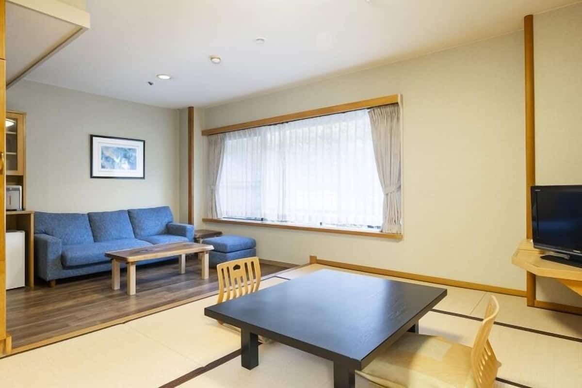 Un espacio habitable compacto con sofá, una mesita, televisor y ventana con cortinas.