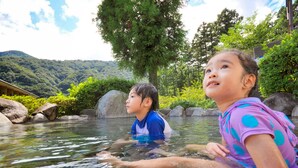 Two children in a natural pool surrounded by rocks and greenery, with a mountainous backdrop. - Hakonenomori Okada (Hakone)