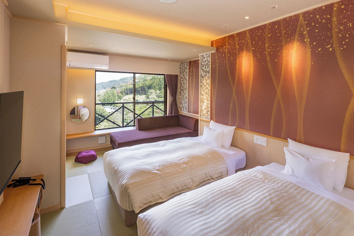 Habitación de hotel con dos camas, televisión, ventana con vistas a zonas verdes y balcón.