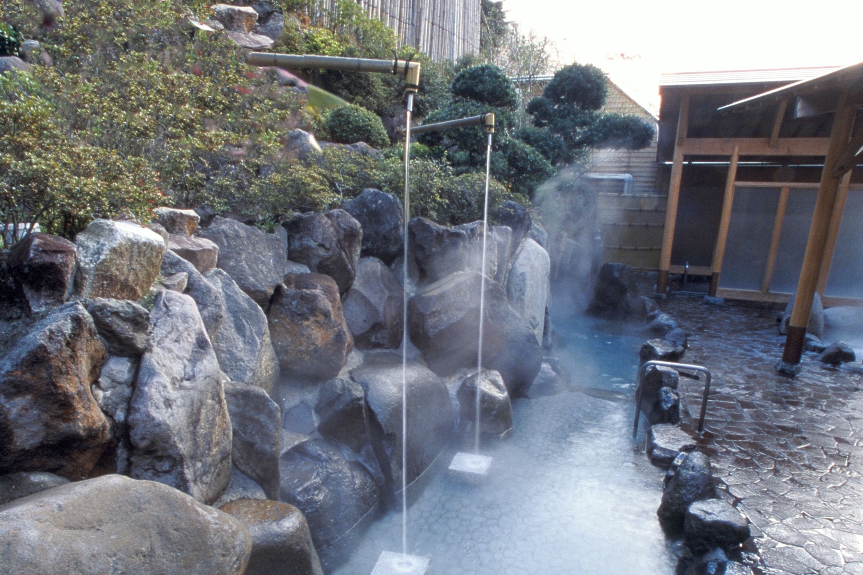 A hot spring area with large rocks, a wooden structure, and a stone pathway.