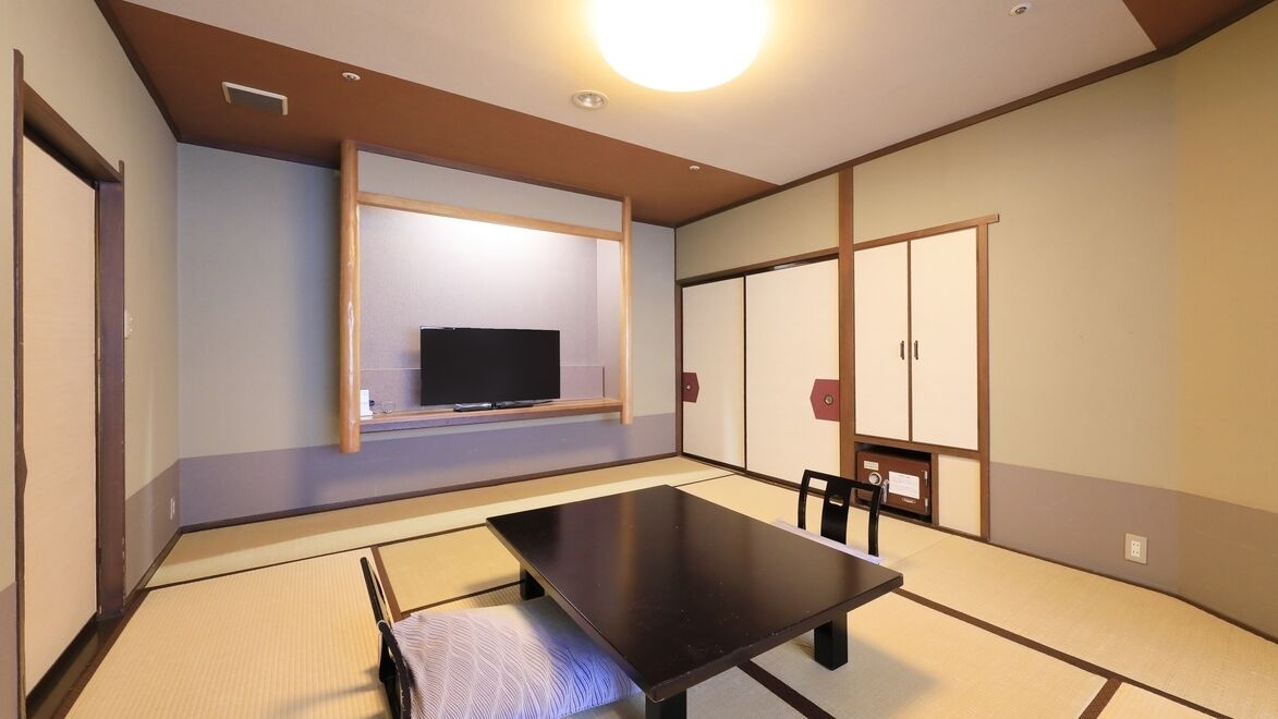 A traditional Japanese room with tatami flooring, a low table, a television, sliding doors, and a ceiling light.
