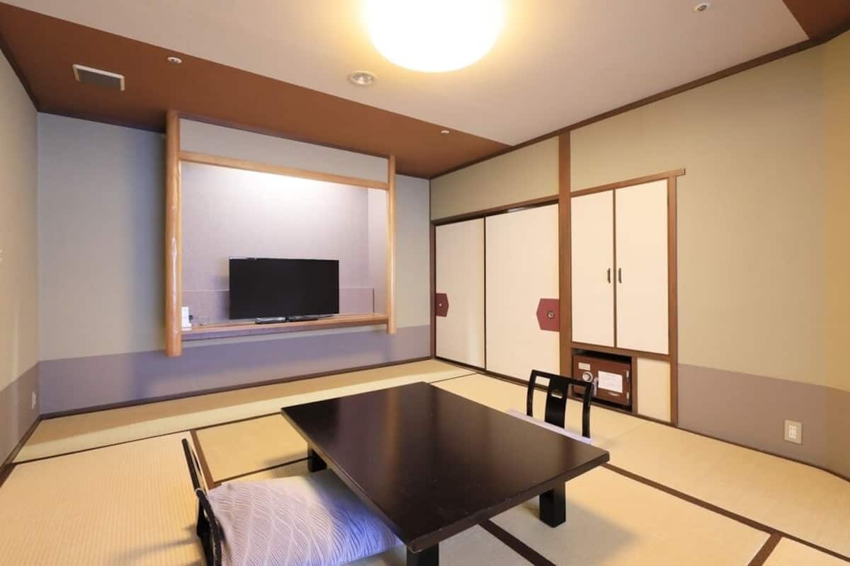 Et traditionelt japansk rum med tatamimåtter, et lavt bord, et fjernsyn, skydedøre og en loftlampe.